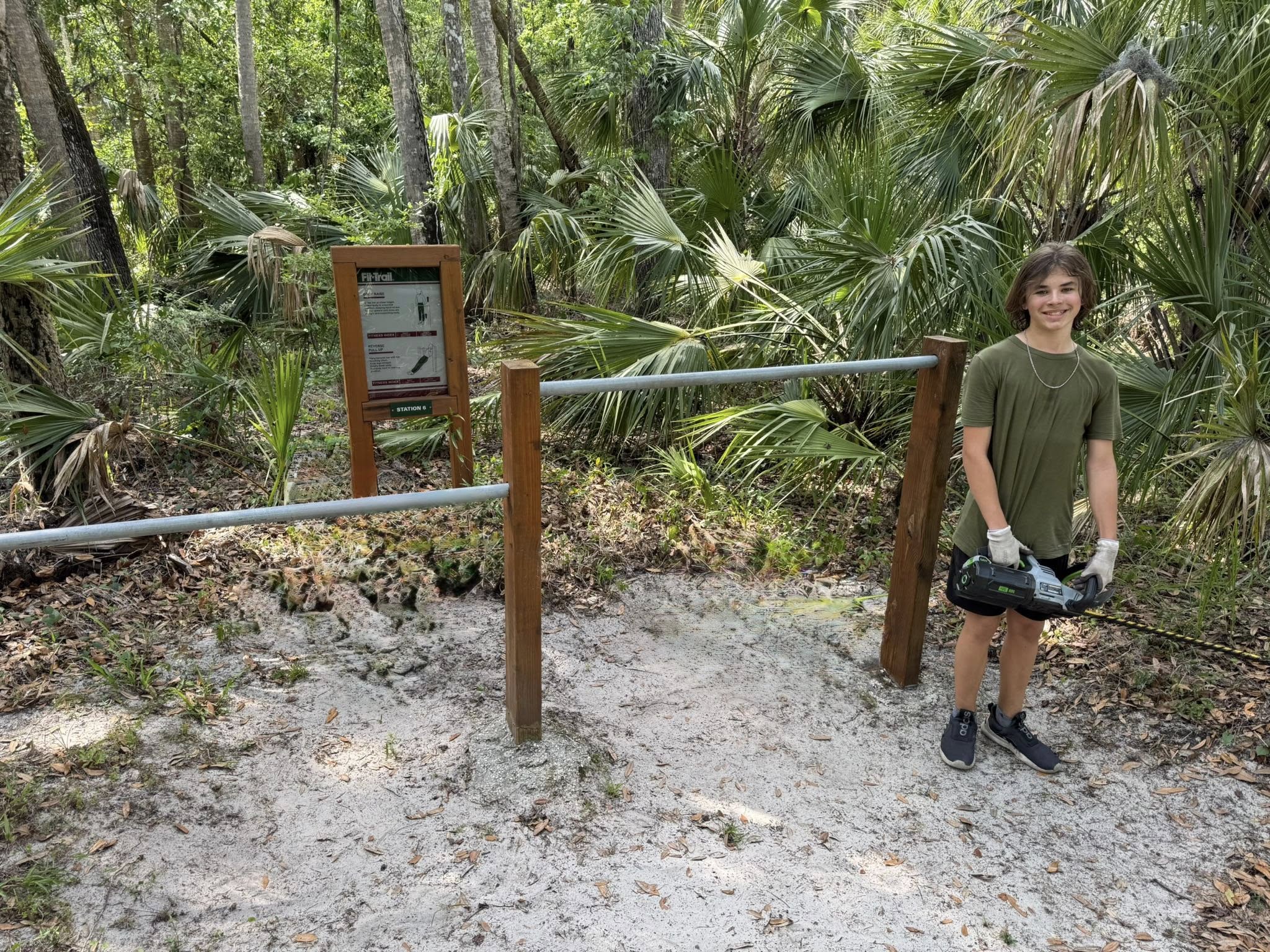 Two young volunteers spreading gravel for a fitness station pad with a wheelbarrow